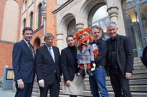 Fünf Personen, ein Mann hält eine Handpuppe, die einen Fuchs darstellt, stehen vor der historischen Fassade des Künstlerhauses in Hannover.