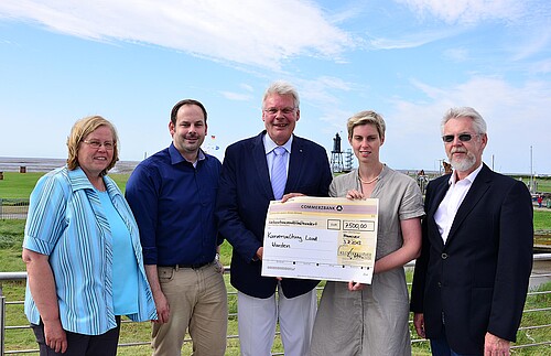 In einer Gruppe von fünf Personen die im Freien stehen halten Klosterkammer-Präsident Hans-Christian und eine Frau einen übergroßen symbolischen Scheck.