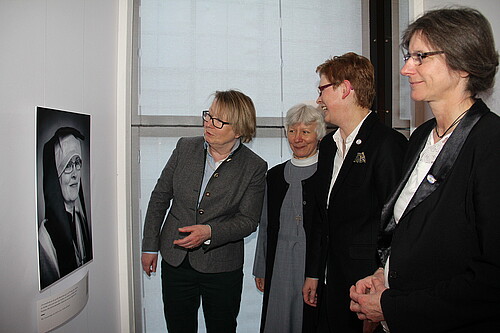 Drei Äbtissinnen und eine Konventualin betrachten ein Schwarz-Weiß-Portrait einer Äbtissin im großen Ornat.