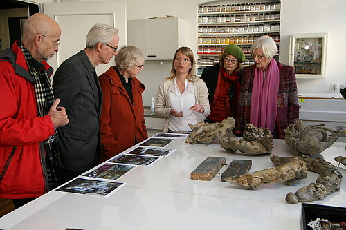 Fünf Personen hören Kirsten Schröder, Restauratorin in der Restaurierungswerkstatt der Klosterkammer Hannover, zu. Sie stehen dabei um einen Tisch in einer Werkstatt gruppiert.