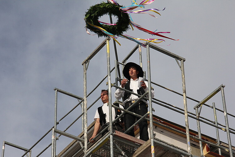 Zwei Zimmermänner in traditioneller Berufsbekleidung stehen auf einem Gerüst.