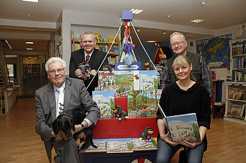 Vier Personen sind rund um ein Bücherregal in Form eines hölzernen Schiffes gruppiert.
