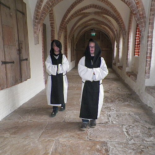 Zwei Kinder gehen in Zisterzienser-Kutten durch den Kreuzgang im Kloster Isenhagen.