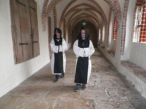 Zwei Kinder gehen in Zisterzienser-Kutten durch den Kreuzgang im Kloster Isenhagen.