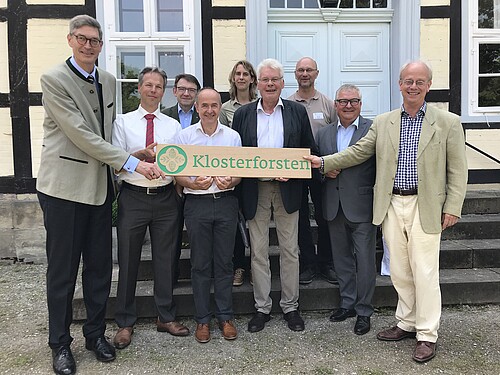 Neun Personen stehen als Gruppe vor einem Fachwerk-Gebäude.