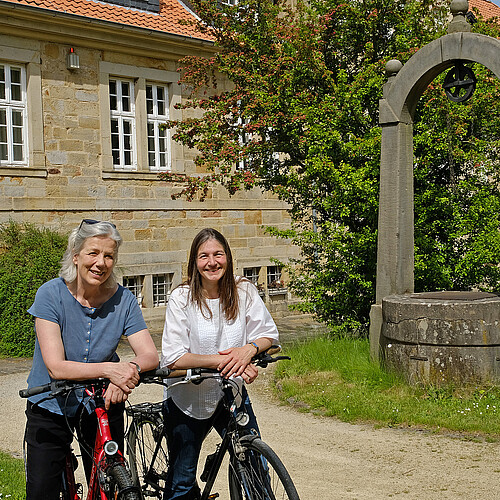 Zwei Frauen stehen mit Fahrrädern in einem Klostergarten