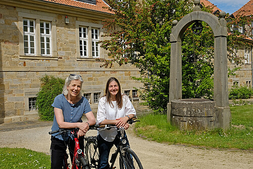 Zwei Frauen stehen mit Fahrrädern in einem Klostergarten