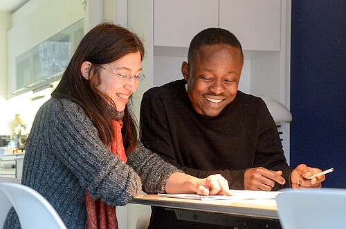 Eine Frau und ein Mann sitzen an einem Tisch und unterhalten sich, vor ihnen liegen Papiere.