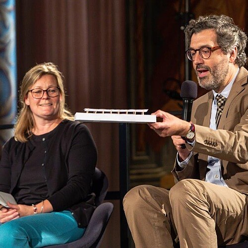 Dr. Stephan Lüttich, Abteilungsleiter Förderungen der Klosterkammer, sitz zusammen mit einer Frau auf einer Bühne und zeigt ein Papier-Modell des Arne Jacobsen Foyers.