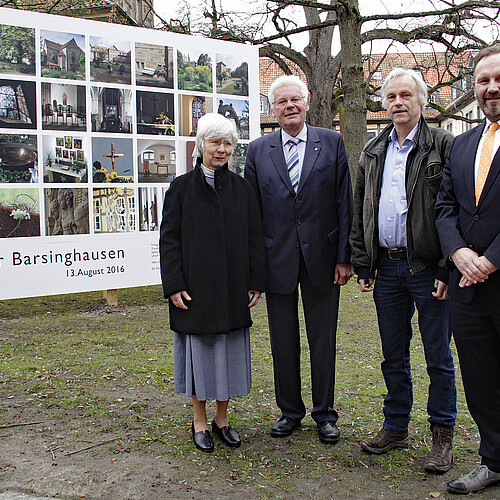 Vier Personen stehen vor einer großformatigen Wand mit Fotografien. Im Hintergrund sind Gebäudeteile des Klosters Barsinghausen zu sehen.