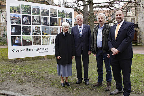 Vier Personen stehen vor einer großformatigen Wand mit Fotografien. Im Hintergrund sind Gebäudeteile des Klosters Barsinghausen zu sehen.