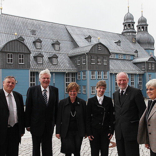 Eine große hölzerne Kirche in blauer Farbe mit grauem Dach - davor steht eine Gruppe von Menschen, darunter Klosterkammer-Präsident Hans-Christian Biallas
