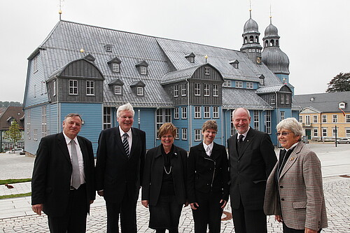 Eine große hölzerne Kirche in blauer Farbe mit grauem Dach - davor steht eine Gruppe von Menschen, darunter Klosterkammer-Präsident Hans-Christian Biallas