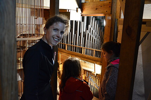 Eine Frau und zwei Kinder im Inneren einer Orgel. Blick auf Orgelpfeifen.