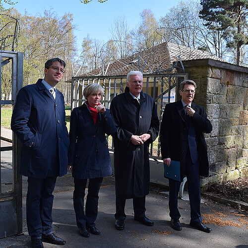 Drei Männer, darunter Klosterkammer-Präsident Hans-Christian Biallas, und eine Frau stehen vor einem geöffneten Tor aus Metallstreben.