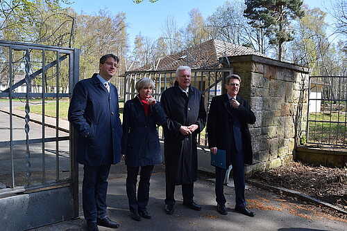 Drei Männer, darunter Klosterkammer-Präsident Hans-Christian Biallas, und eine Frau stehen vor einem geöffneten Tor aus Metallstreben.