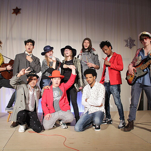 Eine Gruppe Jugendlicher in Kostümen präsentiert sich auf einer Bühne.