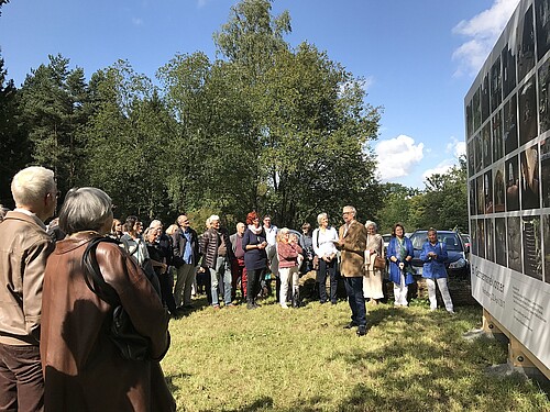 Viele Menschen stehen vor einer Bildtafel.