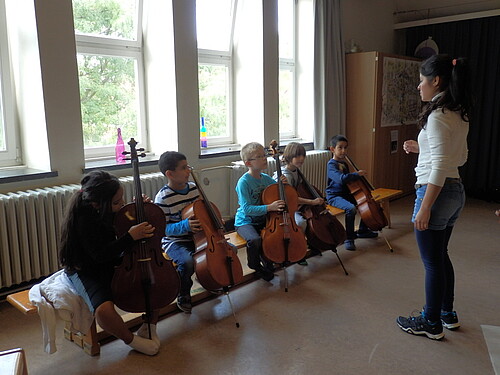 Eine Frau gibt fünf Kindern Cello-Unterricht.