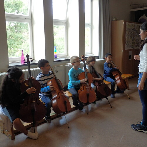 Eine Frau gibt fünf Kindern Cello-Unterricht.