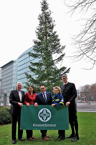 Fünf Personen stehen vor einer Tanne geschmückt mit einer Lichterkette und halten ein Banner mit der Aufschrift Klosterforsten.