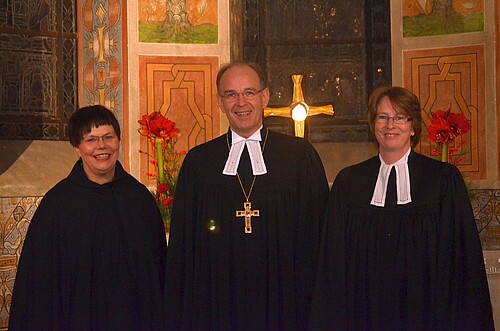 Zwei Frauen, darunter Rosemarie Meding, Äbtissin des Kloster Marienwerder, und ein Mann stehen vor dem Altar der Klosterkirche Marienwerder.