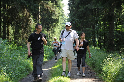 Eine Gruppe mit Fotoapparaten läuft auf einem Waldweg entlang.