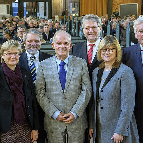 Fünf Männer und zwei Frauen stehen in einer Gruppe vor gefüllten Bänken in einer Kirche.