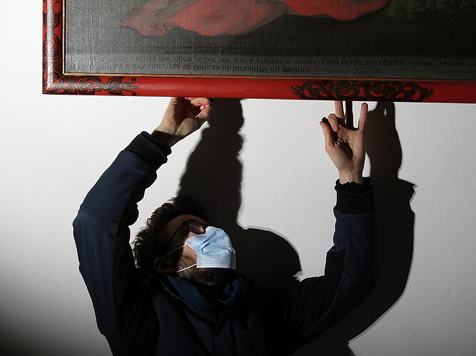 Ein Mann mit einer Mund-Nasen-Maske bring eine Nummer an einem hölzernen Bilderrahmen an.