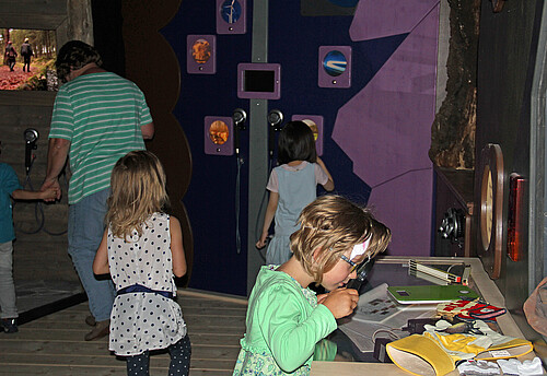 Drei Mädchen schauen sich eine Ausstellung über Fledermäuse an, der Raum ist leicht abgedunkelt.