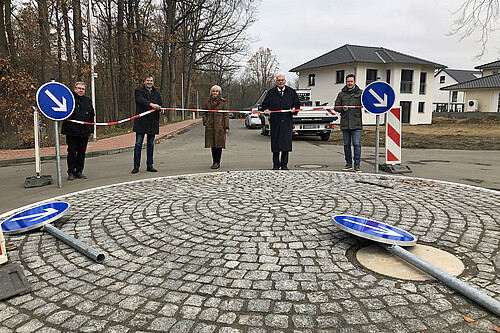 Vier Männer und eine Frau stehen auf einer neu angelegten Straße und halten ein rot-weißes Band in den Händen.