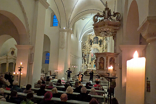 Blick in Kirchinnenraum mit vollbesetzten Bänken, vorne spielen vier Musiker.