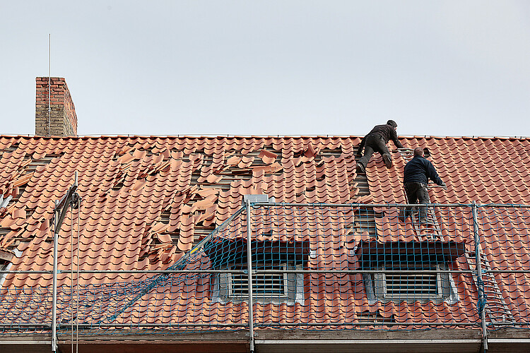Zwei Dachdecker ergänzen in einem roten Ziegeldach einzelne Ziegel und beheben damit Sturmschäden.