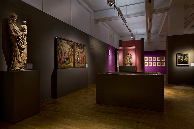 Verschiedene Vitrinen, Statuen und Bilder in einem Raum.