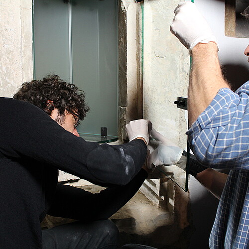 Zwei Männer setzen eine kleine Glastür ein.