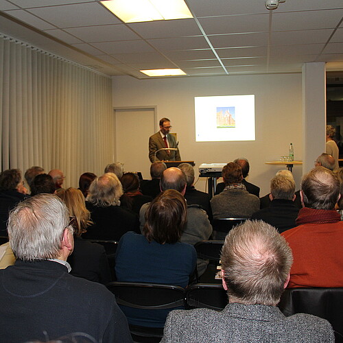 Eine Gruppe von Personen hört einem Redner am Pult zu.