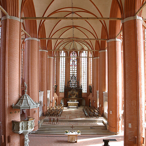 Innenraum einer Kirche, die in braun-roten und hellen Farbtönen gestaltet ist.
