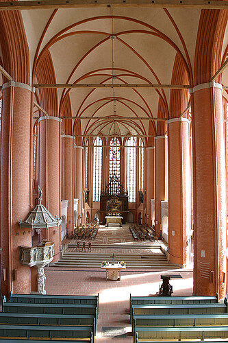 Innenraum einer Kirche, die in braun-roten und hellen Farbtönen gestaltet ist.