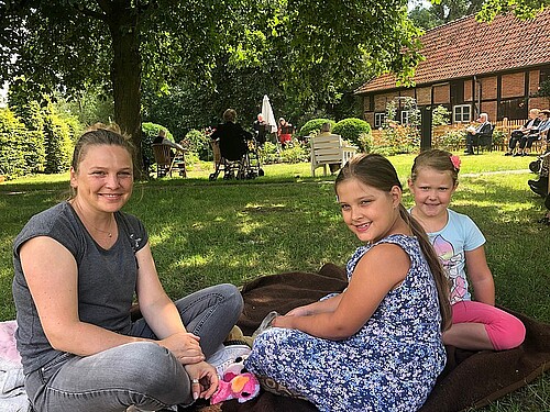 Eine Frau und zwei Mädchen auf einer Decke im Garten.