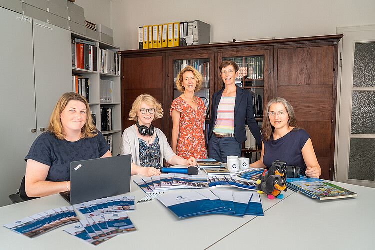 Fünf Frauen stehen oder sitzen im Halbrund um einen Besprechungstisch mit Material zur Öffentlichkeitsarbeit der Klosterkammer.