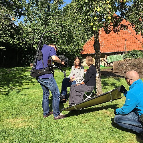 Ein Kamerateam filmt zwei Frauen, darunter Schwester Reinhild von Bibra, Äbtissin des Klosters Wülfinghausen, im Garten unter einem Birnenbaum.