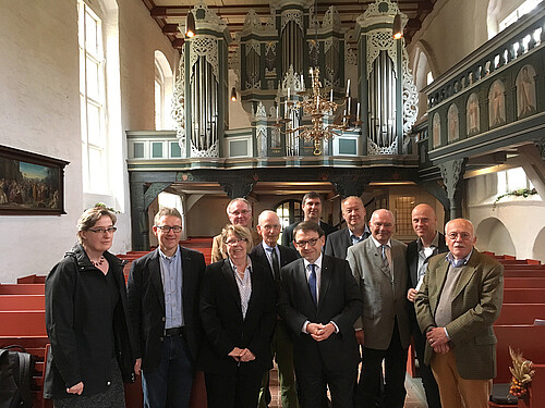 Eine Gruppe von Frauen und Männern, darunter Kammerdirektor Andreas Hesse, stehen in dem Mittelgang der Kirche St. Johannis in Oederquart. Im Hintergrund ist eine kunstvoll gestaltete historische Orgel zu sehen.