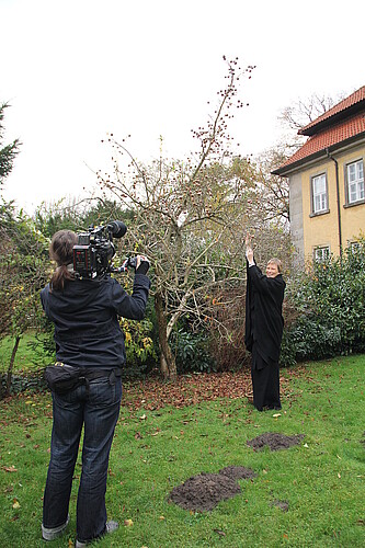 Bärbel Görcke, Äbtissin des Klosters Mariensee, steht unter einem Apfelbaum und wird dabei von einer weiteren Frau mit einer Fernsehkamera gefilmt.