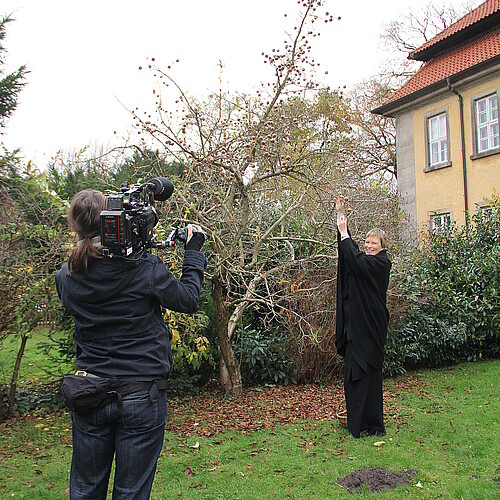 Bärbel Görcke, Äbtissin des Klosters Mariensee, steht unter einem Apfelbaum und wird dabei von einer weiteren Frau mit einer Fernsehkamera gefilmt.
