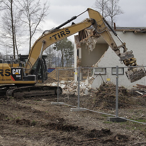 Ein Bagger reißt ein eingezäuntes Haus ein.