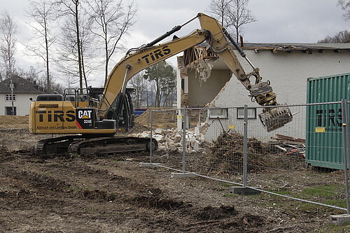 Ein Bagger reißt ein eingezäuntes Haus ein.