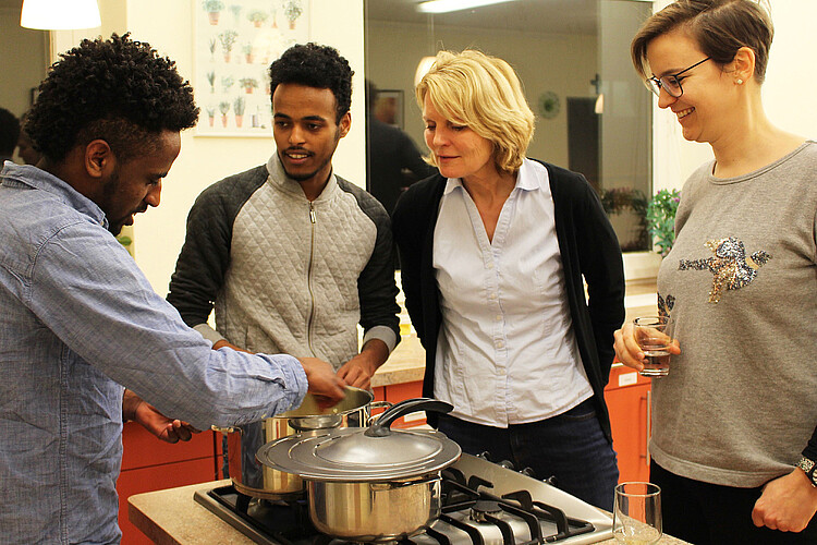 Zwei junge Männer und zwei Frauen stehen gemeinsam um einen Herd herum.