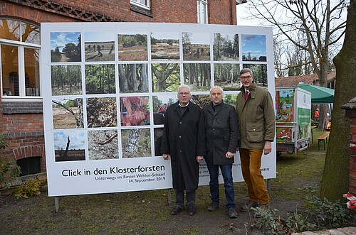 Drei Männer vor einer Fotowand.