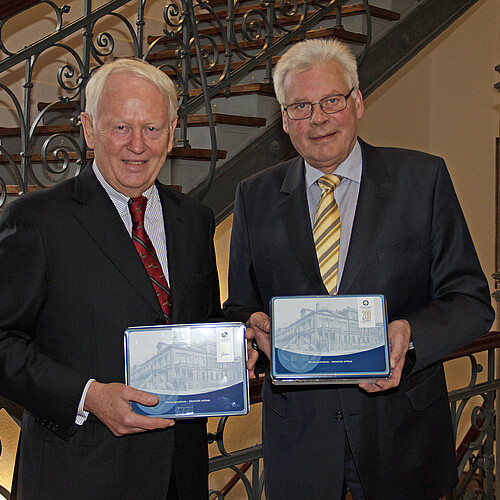 Zwei Herren stehen nebeneinander und halten jeweils eine Keksdose in der Hand.