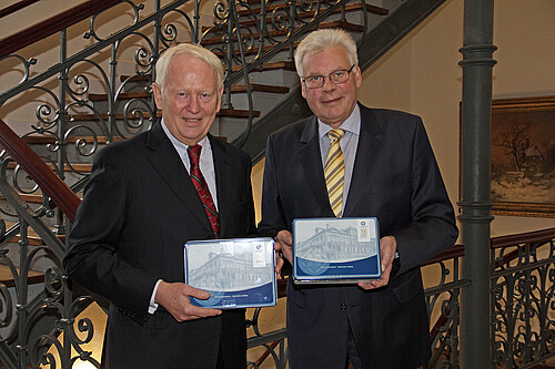 Zwei Herren stehen nebeneinander und halten jeweils eine Keksdose in der Hand.